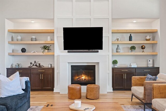 living area featuring built in shelves, a glass covered fireplace, and light wood-style flooring