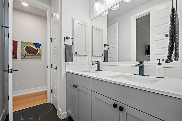 full bathroom with wood finished floors, a sink, baseboards, and double vanity