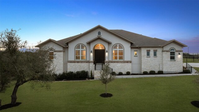 view of front facade featuring a shingled roof, stone siding, a front lawn, and stucco siding