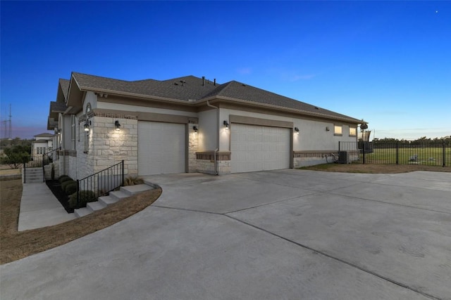 view of front of property featuring stucco siding, an attached garage, fence, stone siding, and driveway