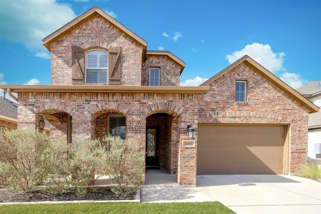 french country inspired facade with concrete driveway, brick siding, and an attached garage