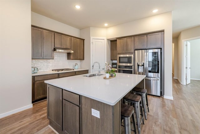 kitchen featuring a center island with sink, a breakfast bar area, stainless steel appliances, backsplash, and a sink