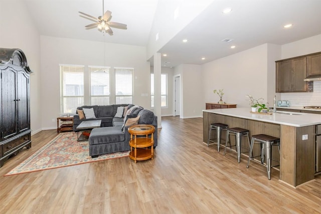 living area with high vaulted ceiling, light wood-style flooring, recessed lighting, a ceiling fan, and baseboards