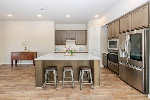 kitchen featuring a kitchen island, visible vents, appliances with stainless steel finishes, decorative backsplash, and a kitchen bar