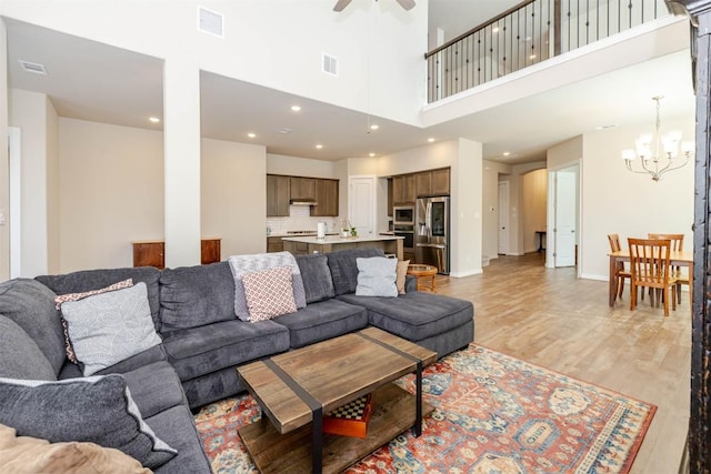 living room featuring light wood-type flooring, visible vents, and ceiling fan with notable chandelier