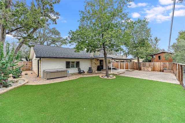 rear view of house featuring a fenced backyard, a lawn, a hot tub, and a patio