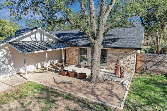 view of front of home with metal roof, a patio area, stone siding, and a shingled roof