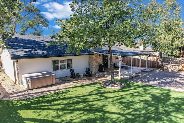 rear view of property featuring a shingled roof, a hot tub, fence, a yard, and a patio