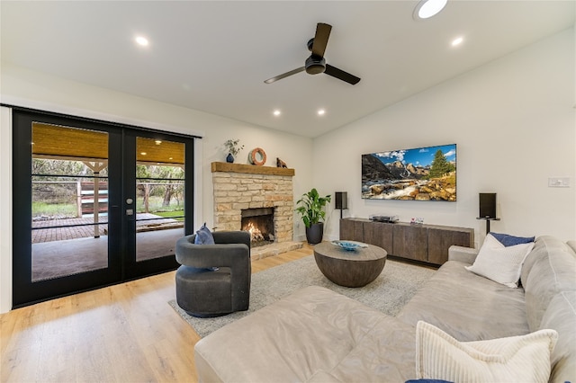 living room with light wood-type flooring, a stone fireplace, french doors, and vaulted ceiling