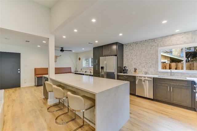 kitchen with light wood finished floors, a sink, light countertops, appliances with stainless steel finishes, and a center island