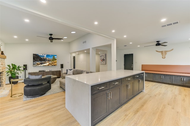 kitchen with ceiling fan, visible vents, a stone fireplace, and light wood-style flooring