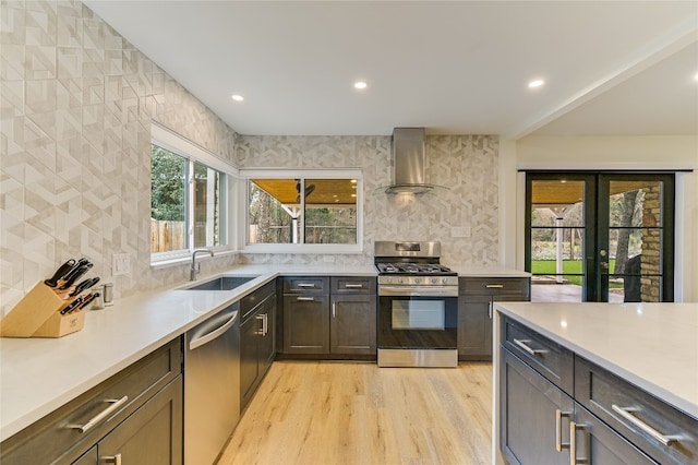 kitchen featuring a sink, appliances with stainless steel finishes, light countertops, and wall chimney range hood