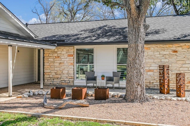 exterior space featuring roof with shingles, a standing seam roof, stone siding, a patio area, and metal roof