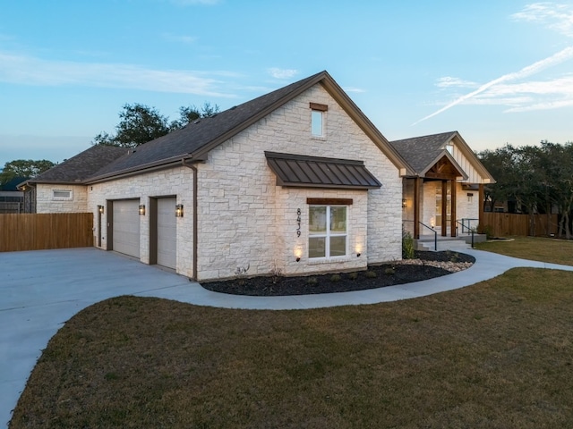 view of front facade with an attached garage, fence, concrete driveway, a standing seam roof, and a front yard