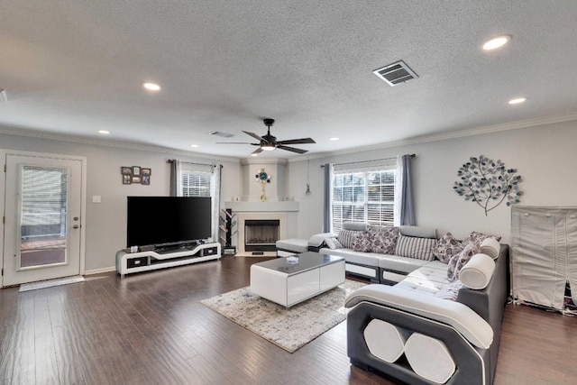 living area with a textured ceiling, a fireplace, wood finished floors, visible vents, and crown molding