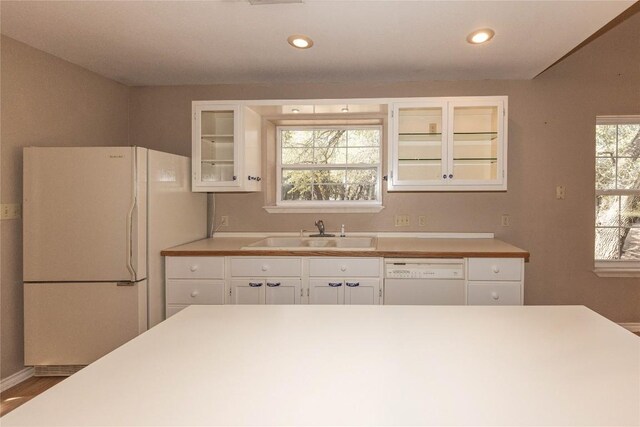 kitchen featuring white appliances, white cabinets, glass insert cabinets, light countertops, and a sink