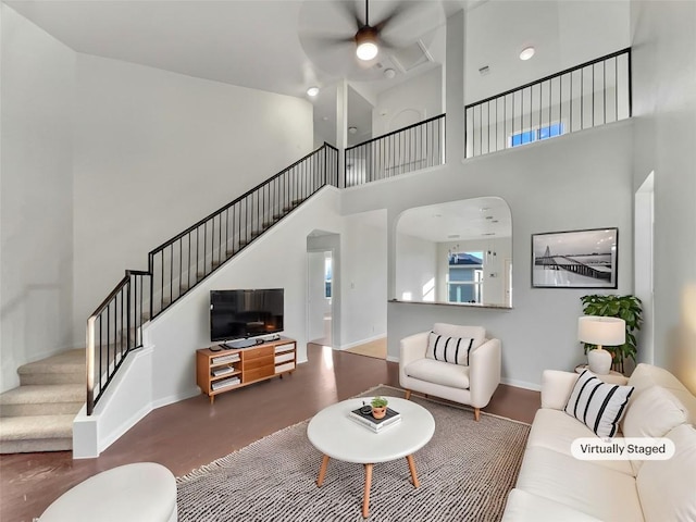 living area featuring stairway, a ceiling fan, baseboards, and a towering ceiling