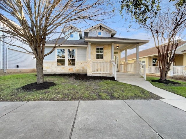 view of front facade featuring stone siding, covered porch, a front yard, and roof with shingles