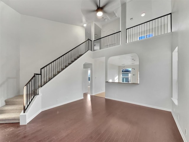 unfurnished living room with wood finished floors, stairway, a high ceiling, baseboards, and ceiling fan