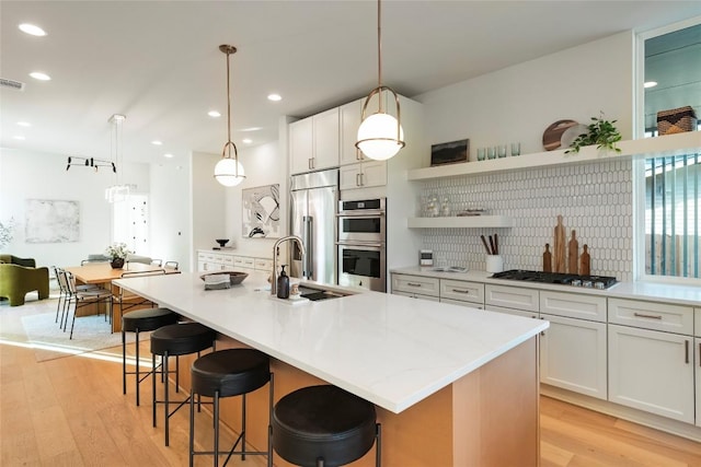 kitchen with light wood finished floors, visible vents, appliances with stainless steel finishes, open shelves, and a sink