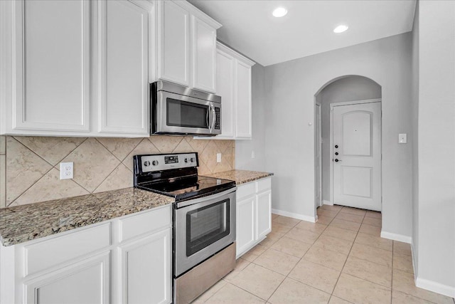 kitchen with arched walkways, white cabinets, light stone countertops, stainless steel appliances, and backsplash