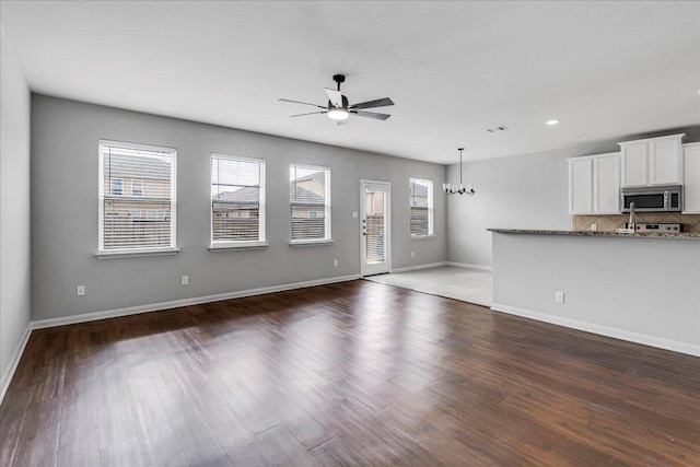 unfurnished living room with a wealth of natural light, baseboards, wood finished floors, and ceiling fan with notable chandelier