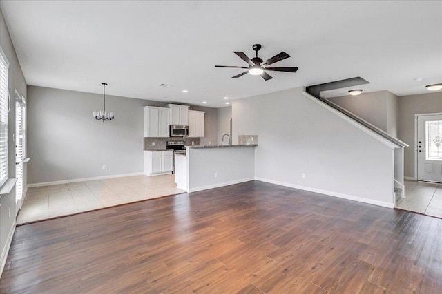 unfurnished living room featuring recessed lighting, baseboards, wood finished floors, and ceiling fan with notable chandelier