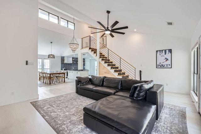 living room featuring visible vents, a ceiling fan, wood finished floors, stairs, and high vaulted ceiling