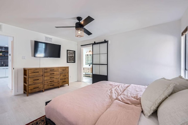 bedroom featuring a ceiling fan, wood finished floors, visible vents, and a barn door