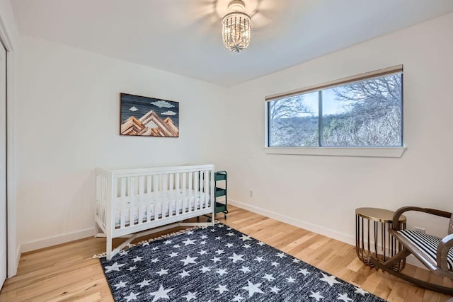 bedroom with a notable chandelier, a nursery area, wood finished floors, and baseboards