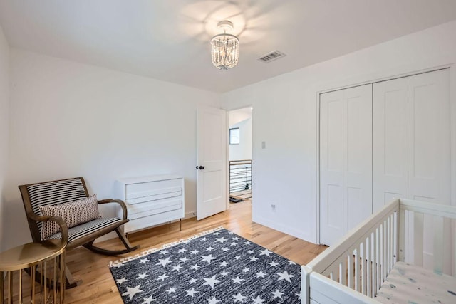 bedroom featuring a closet, visible vents, light wood finished floors, and an inviting chandelier