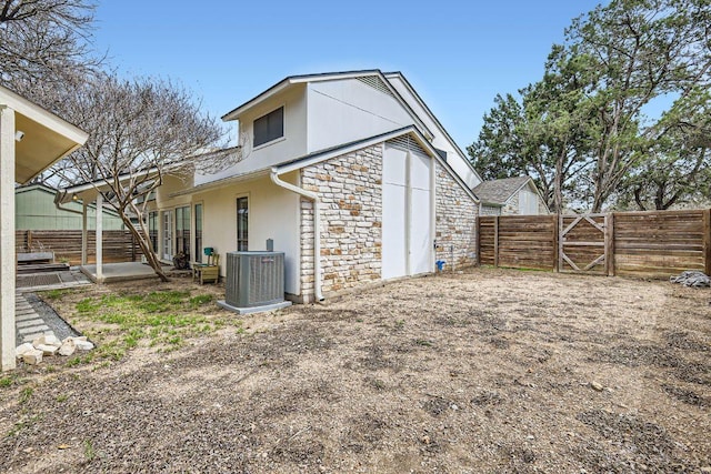 rear view of house featuring stucco siding, a gate, central AC, stone siding, and a fenced backyard