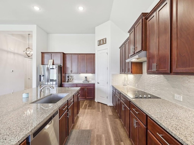 kitchen featuring dark wood finished floors, light stone counters, appliances with stainless steel finishes, under cabinet range hood, and a sink