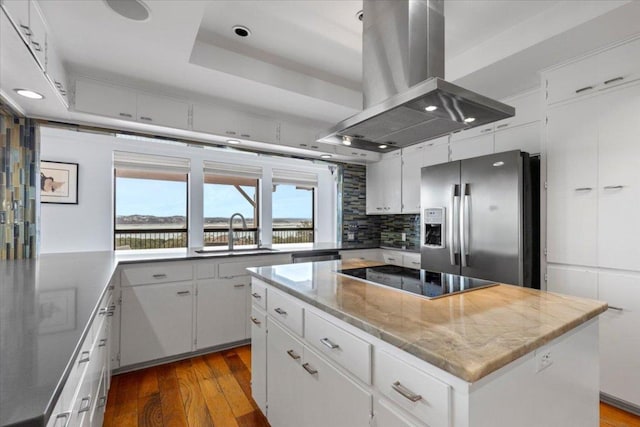 kitchen featuring a tray ceiling, island exhaust hood, black electric stovetop, a kitchen island, and stainless steel fridge with ice dispenser