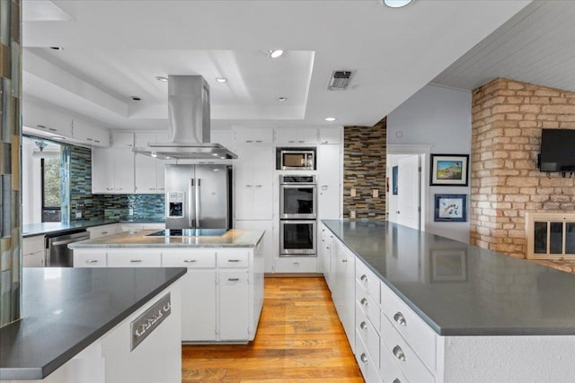 kitchen with island exhaust hood, dark countertops, decorative backsplash, appliances with stainless steel finishes, and a kitchen island