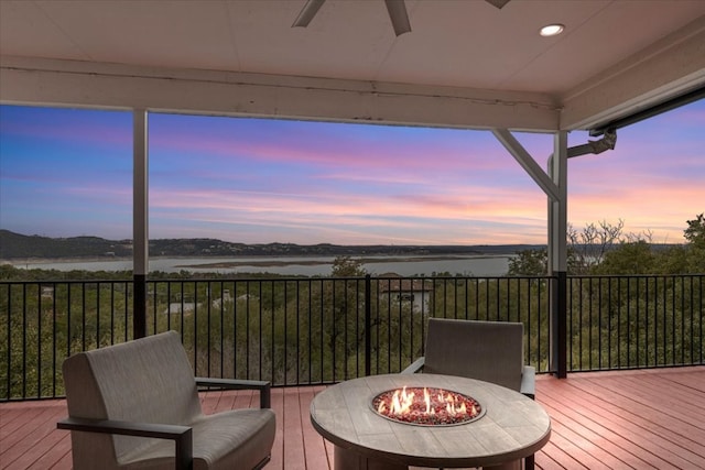 wooden terrace with a water view, an outdoor fire pit, and ceiling fan