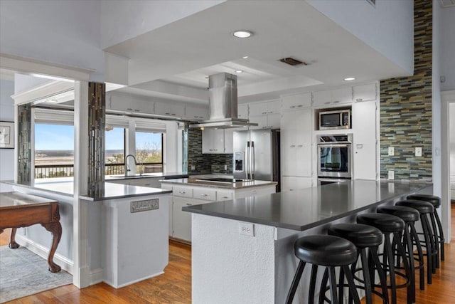 kitchen featuring visible vents, island range hood, dark countertops, a peninsula, and stainless steel appliances