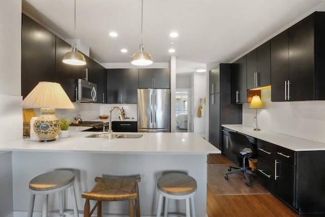 kitchen featuring a sink, a peninsula, appliances with stainless steel finishes, and dark cabinets