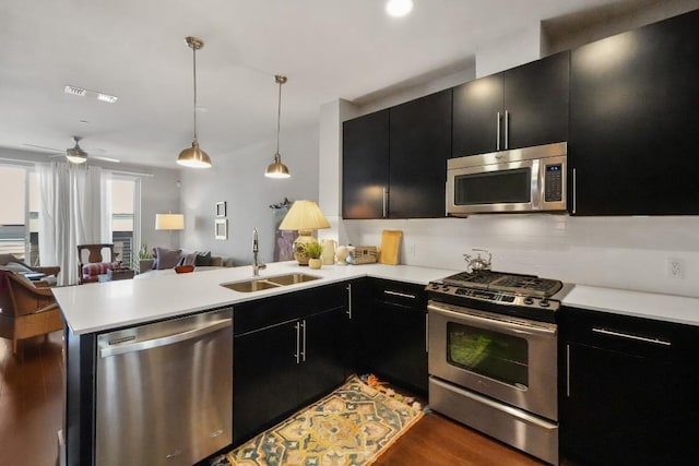 kitchen featuring appliances with stainless steel finishes, open floor plan, a sink, dark cabinetry, and a peninsula