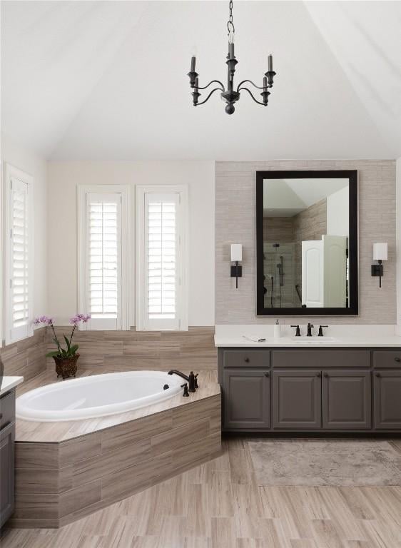 bathroom with a stall shower, lofted ceiling, a garden tub, an inviting chandelier, and vanity