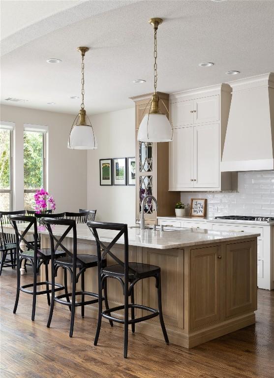 kitchen with a breakfast bar area, custom range hood, backsplash, dark wood-style floors, and pendant lighting