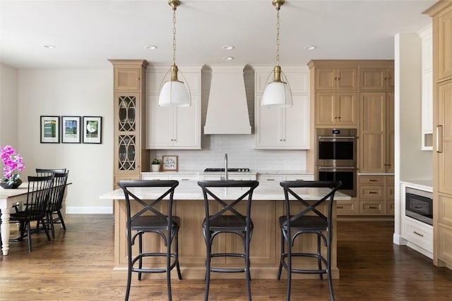 kitchen with dark wood finished floors, an island with sink, stainless steel appliances, light countertops, and premium range hood