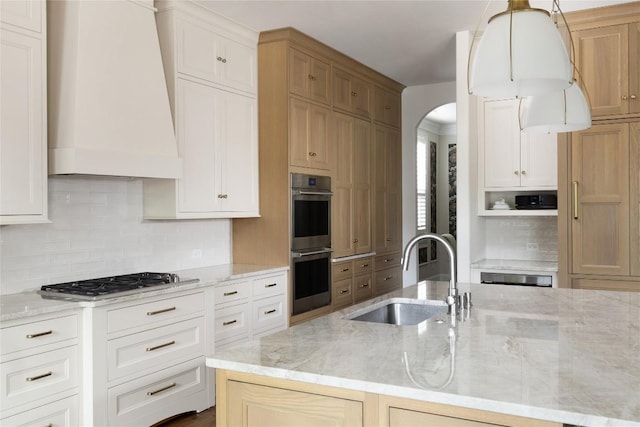 kitchen with custom range hood, light stone counters, appliances with stainless steel finishes, a sink, and backsplash