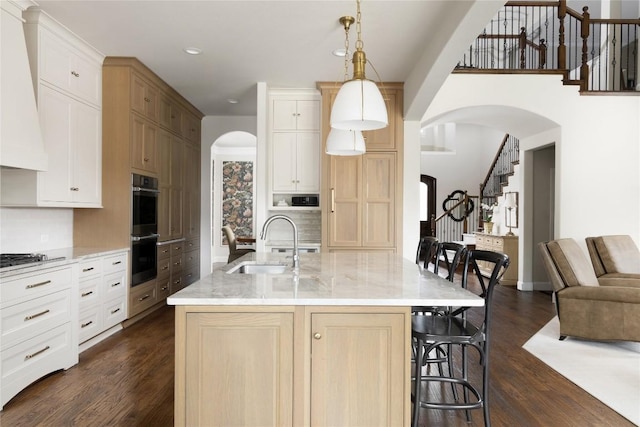 kitchen featuring stainless steel double oven, a sink, dark wood finished floors, wall chimney range hood, and a kitchen bar