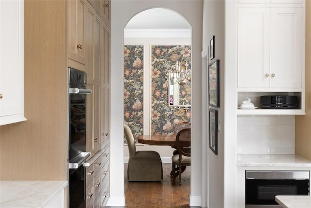 interior space featuring dark wood-type flooring, arched walkways, crown molding, and baseboards