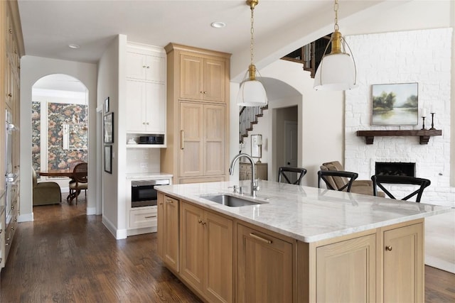 kitchen featuring arched walkways, dark wood-style flooring, a fireplace, a sink, and light stone countertops