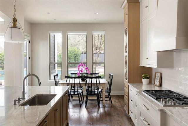 kitchen with wall chimney range hood, a sink, a wealth of natural light, and stainless steel gas stovetop