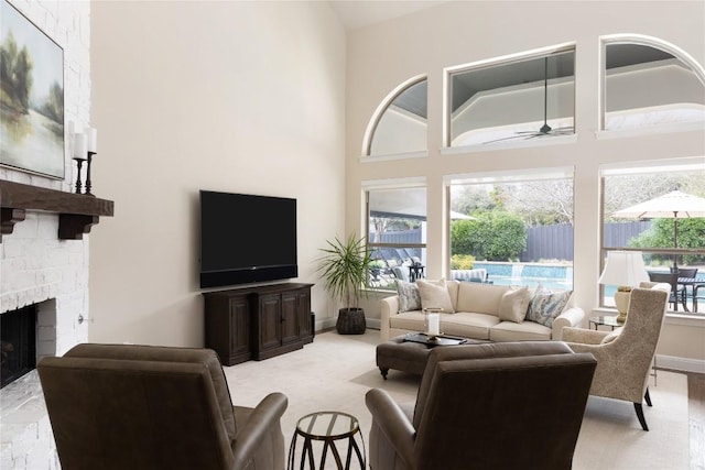 living area featuring ceiling fan, a stone fireplace, a towering ceiling, baseboards, and carpet