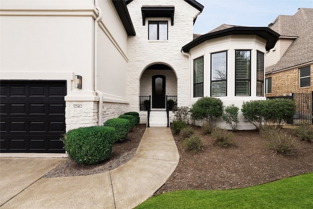 property entrance with a garage, stone siding, and fence