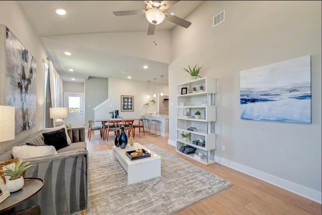 living area featuring vaulted ceiling, light wood-style flooring, visible vents, and baseboards